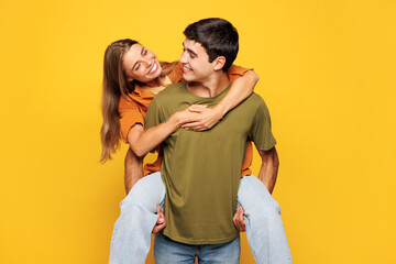 Fototapeta premium Young fun couple two friends family man woman wear shirt casual clothes together giving piggyback ride to joyful sit on back isolated on pastel plain light yellow background studio. Lifestyle concept