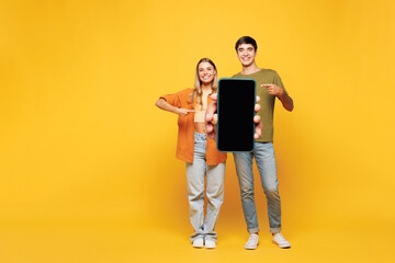 Naklejka premium Full body young couple two friend family man woman wear casual clothes together hold use mobile cell phone, blank screen workspace area isolated on pastel plain light yellow color background studio.