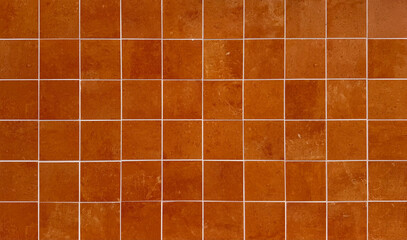 Rustic terracotta square tile wall texture with white grout lines. Traditional ceramic floor or wall tiling background in earthy orange and brown tones for interior or exterior architectural design.