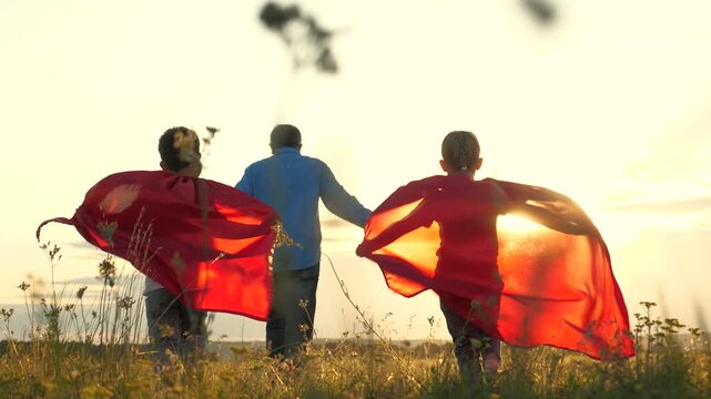 little children father dream becoming superheroes. Son daughter play with father street sunset, red raincoats flutter wind. Boy girl imagines himself superhero motion runs across green field play game