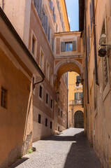 Fototapeta premium Quiet narrow street in the historic center of Rome with stone pavement and arch connecting old buildings.