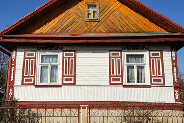 Obraz premium Traditional wooden countryside house facade with decorative window shutters. Rural village home exterior with fence and colorful wooden architecture. Sunny residential building background.