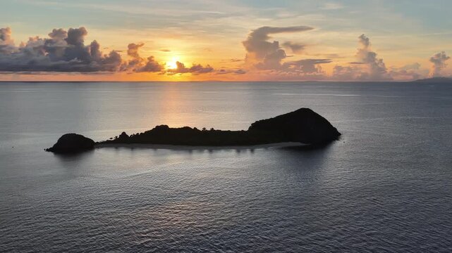A serene sunrise silhouettes a small island in the Vatu-i-ra seascape in Fiji. This area is a marine protected area known for its high biodiversity and is a destination for divers and snorkelers.
