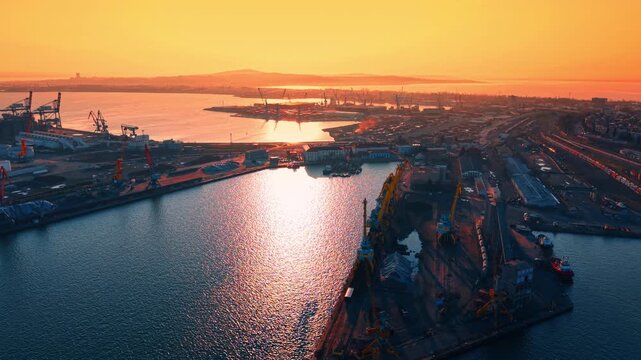Commercial harbor with cranes and shipping facilities at dusk. High angle view of maritime terminal, water basins and industrial equipment.