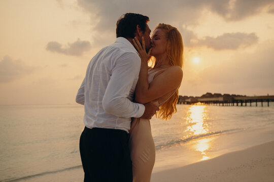 Dreamy honeymoon moment of a couple kissing on a beautiful beach at sunset