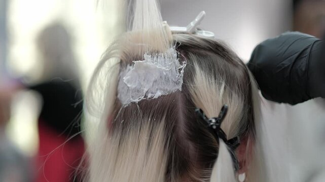 Professional hairdresser applying bleach to the roots of a blonde woman's hair in a beauty salon