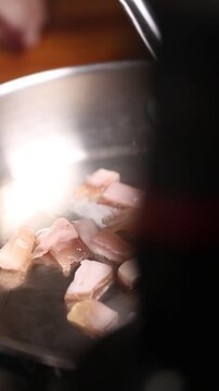 Cocinero profesional con guantes de l&aacute;tex negro fr&iacute;e peque&ntilde;os trozos de grasa de jam&oacute;n ib&eacute;rico en una sart&eacute;n de acero inoxidable, generando un chisporroteo intenso y aromas ricos durante la cocci&oacute;n.