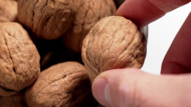 Hand picking walnut from ceramic kitchen bowl with whole nuts in natural shell. Healthy food ingredient and nutrition concept.