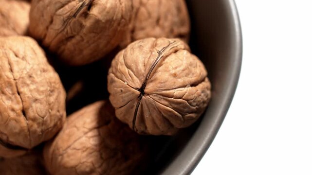 A spinning walnut falling into a bowl of unshelled nuts on a white table