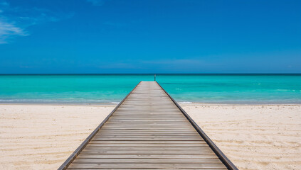 Fototapeta premium Wooden pier leading to turquoise ocean waters and sandy beach under a clear blue sky
