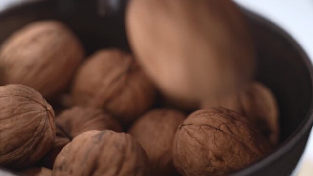 Hand selecting walnuts in shell from bowl on white table. Healthy snack concept.