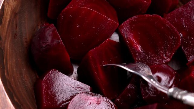 Shiny steel fork pierces a piece of sliced ​​beetroot in rustic wooden bowl. Dietary fiber nutrition
