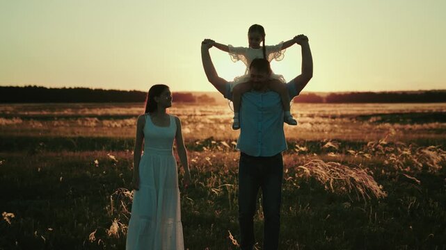 Uncle takes walk carrying niece on shoulders giving real parents break. Uncle teaches little niece to play plane and enjoys life while parents at work. Uncle plays with niece near own wife at sunset