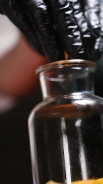 Un cocinero profesional con guantes de l&aacute;tex negro introduce trozos de melocot&oacute;n y tiras de piel de naranja en un bote de cristal transparente, preparando los ingredientes para elaborar un alm&iacute;bar