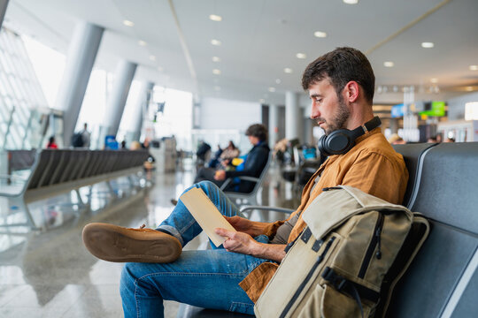 Male traveler waiting in airport terminal reading boarding pass