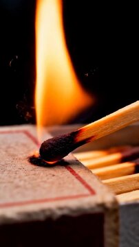 Vertical video: Striking match head creating sparks on matchbox striker, igniting flame for light