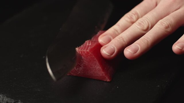 Close-up view of a skilled chef's hands precisely slicing a fresh, vibrant red tuna fillet into thin pieces, preparing high-quality ingredients for a gourmet japanese seafood dish