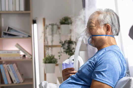 Elderly senior Asian man wearing oxygen breathing mask indoors room feeling tired sick unwell health issue medical care treatment respiratory therapy clinic recovery disease asthma inhaler