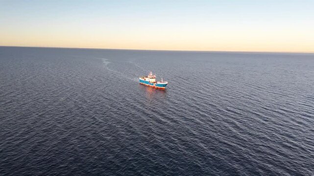 Aerial flies from the Punta Arenas shore toward an industrial fishing vessel, tilting down for a detailed close-up of the ship's deck and equipment in the blue waters of Chile