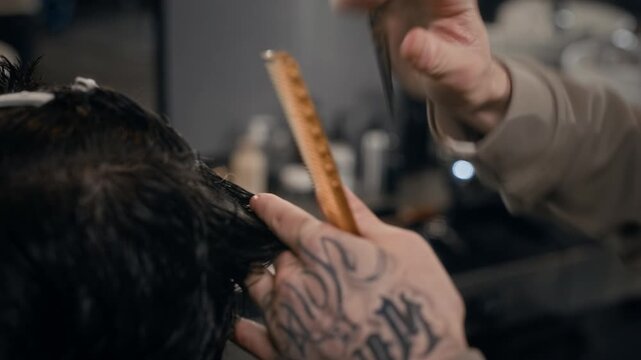 Close up of unrecognizable barber cutting wet hair of client, using comb and professional scissors in barbershop