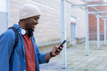 African American man standing, checking smartphone on campus with backpack, headphones, copy space