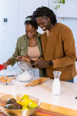 African American couple sifting flour with metal sieve into glass mixing bowl at kitchen island