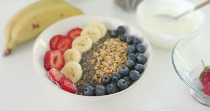 Camera pulling back to reveal white bowl with fruit, chia stripe, yogurt and bananas on countertop