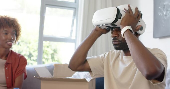 Couple watching man holding, lowering and adjusting white VR headset after unboxing on couch