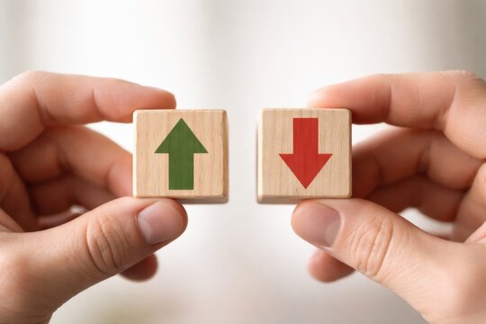 Two hands hold wooden blocks, one showing a green upward arrow and the other a red downward arrow, symbolizing increase and decrease or positive and negative trends.