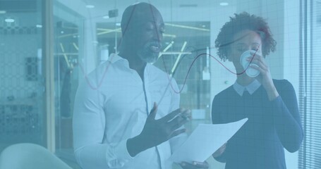 Discussing colleagues in business attire with docs and cup at office glass partition with red graph