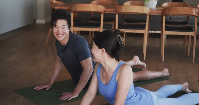 Couple practicing yoga pressing up from prone into cobra on green mats, bonding near dining table