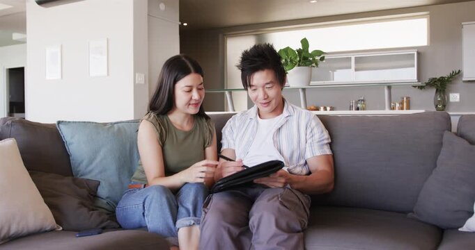 Vertical video: Diverse couple sitting on gray sofa, man handing pen in folio while she signing