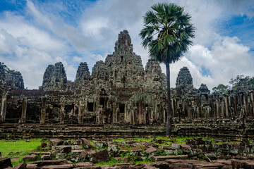 Naklejka premium Ancient Bayon Temple ruins with palm tree in Angkor Thom