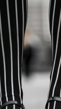 Vertical video: Shifting weight, legs in striped hosiery walking on paved sidewalk with Mary Janes