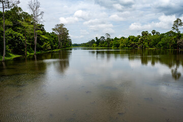Naklejka premium Calm reflective lake surrounded by tropical forest in Siem Reap