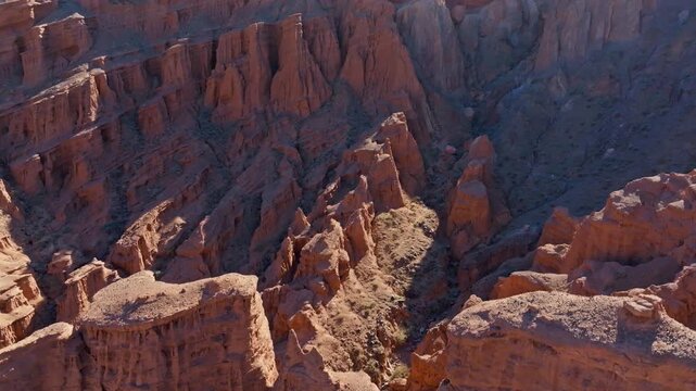 Aerial view of sandstone canyons in arid landscape of Kyrgyzstan. Rugged rock strata showcase natural beauty under bright daylight, descending to closeup view on an intricate slope.