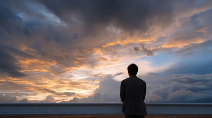 Fototapeta premium A solitary figure stands on a railing gazing at a dramatic sky filled with colorful clouds during sunset or sunrise