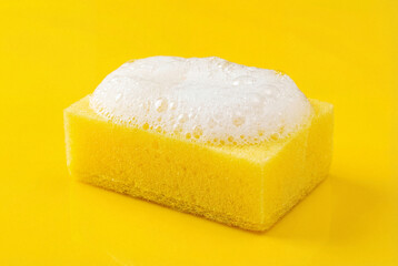 Yellow cleaning sponge with white soap foam on a yellow background
