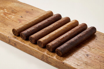 A row of premium hand rolled cigars with different wrapper shades on a wooden board
