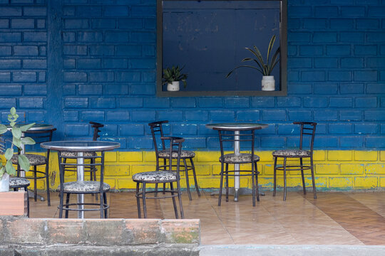 Mesas y sillas de caf&eacute; frente a una pared de ladrillo azul y amarillo.