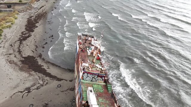 Aerial pulls out from a top-down view of the rusted deck of the Magallanes III shipwreck, revealing the crashing waves of the Strait of Magellan and the sandy shore of Punta Arenas, Chile