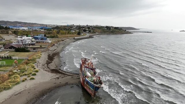Aerial moves forward toward the abandoned factory ship Magallanes III in Punta Arenas, tilting down for a detailed close-up of the rusted industrial deck and bird-covered equipment