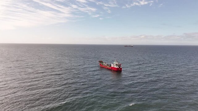 Aerial moves forward toward the red and white multipurpose vessel Anan in the Strait of Magellan near Punta Arenas, tilting down to reveal its open industrial deck and equipment