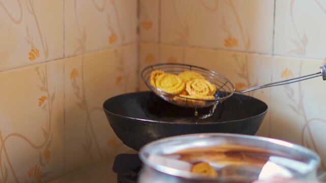 Closeup shot of Indian woman hand deep frying snacks in a restaurant kitchen. Chef putting fried Chakri in steel container. Authentic Indian street food is being prepared. Indian snacks.