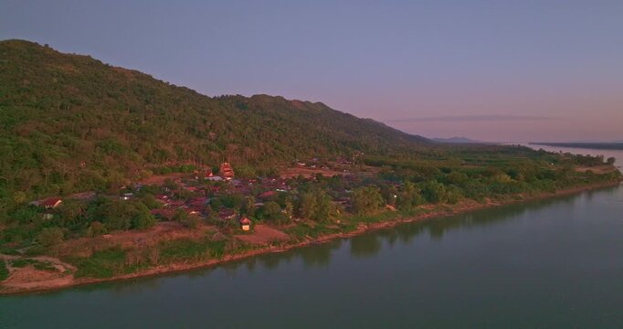 Drone perspective of Pak Kading at dusk, where warm orange and pink skies illuminate the river landscape and rural surroundings of Bolikhamxay Province.