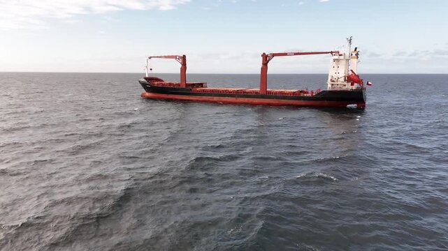 Aerial moves forward toward the Chilean-flagged container and cargo ship in the Strait of Magellan, tilting down to reveal a close-up of the red cargo deck and industrial cranes