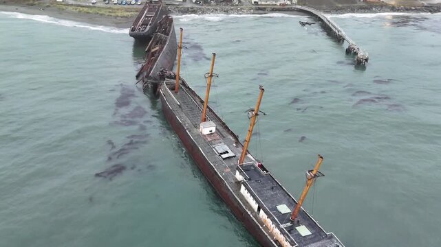 Overhead aerial shot moving forward over the rusted hulls of the beached Mu&ntilde;oz Gamero, Hipparchus, and Falstaff shipwrecks, serving as a breakwater in Punta Arenas, Chile