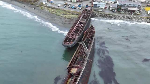 Aerial moves forward over the Strait of Magellan to reveal the rusted iron hulls of the Mu&ntilde;oz Gamero and Hipparchus, beached as a functional breakwater near Punta Arenas, Chile