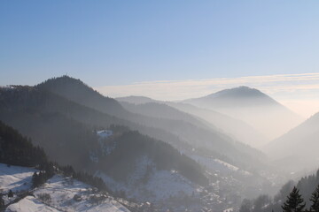 Obraz premium Panoramic view of misty mountains covered in snow during a cold winter morning