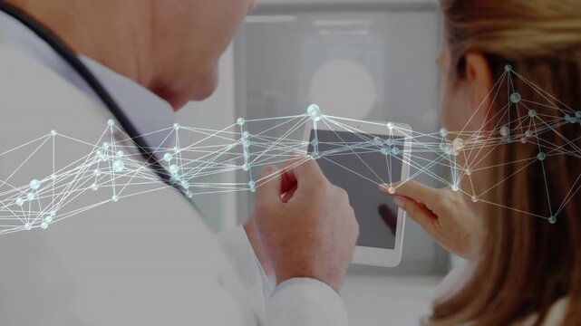 Senior MD holding tablet while peer tapping screen activating animated network showing health data